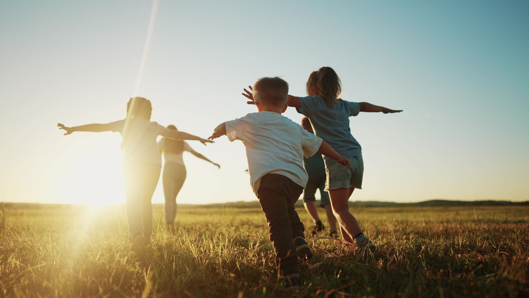 Children running through the field towards the sunset